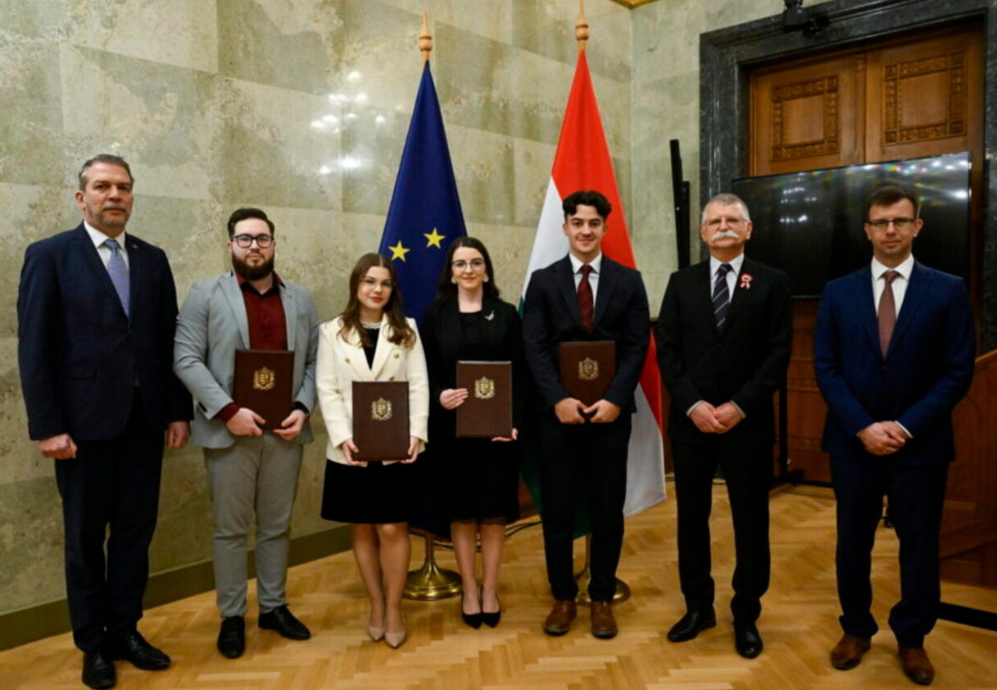 Zupkó Gábor, az Európai Unió magyarországi képviseletének vezetője (b1), Kövér László, az Országgyűlés elnöke (j2) és Bóka János európai uniós ügyekért felelős miniszter (j), díjátadók, valamint Szegecs Attila, a Pázmány Péter Katolikus Egyetem jogászképzésének hallgatója (b2), Sztrein Daniella Sztella, a Károli Gáspár Református Egyetem jogászképzésének hallgatója (b4), Sümegi Szandra, a Szegedi Tudományegyetem jogászképzésének hallgatója (b3) és Nagy Levente, a Debreceni Egyetem gazdálkodási és menedzsment szakos hallgatója (j3), díjazottak a Magyarország és a közép-európai térség az Európai Unióban, az Európai Unió a világban címmel főiskolai és egyetemi hallgatóknak meghirdetett pályázat díjátadó ünnepségén az Országház Delegációs termében 2026. március 16-án